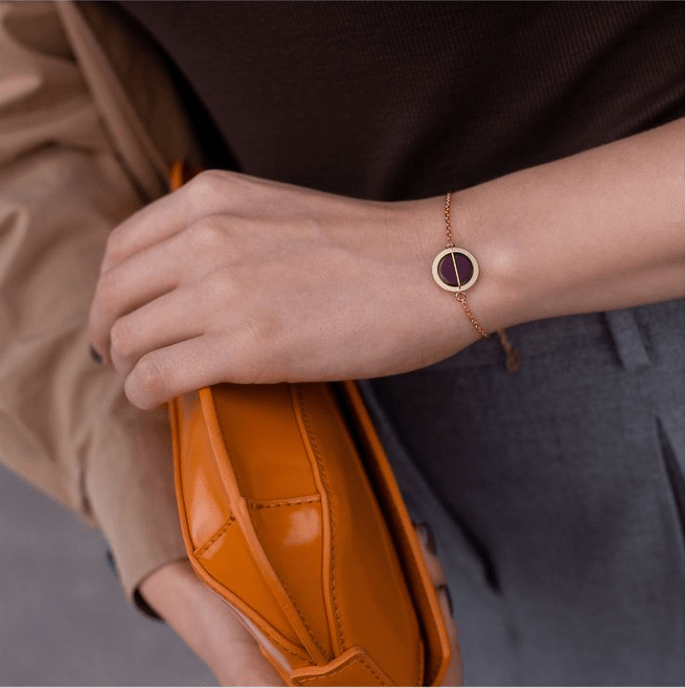 Na zdjęciu widoczne kobiece ręce trzymające pomarańczową torebkę. Na lewej ręce pozłacana bransoletka z bursztynem. 